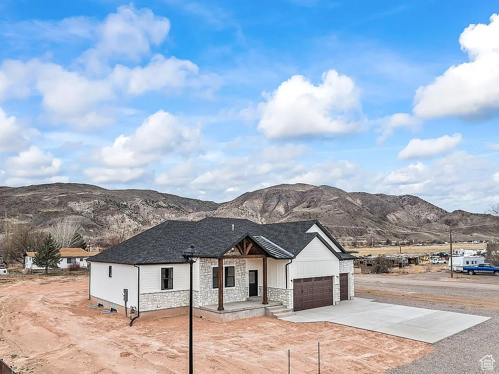 View of front of property featuring a mountain view, stone siding, an attached garage, and driveway
