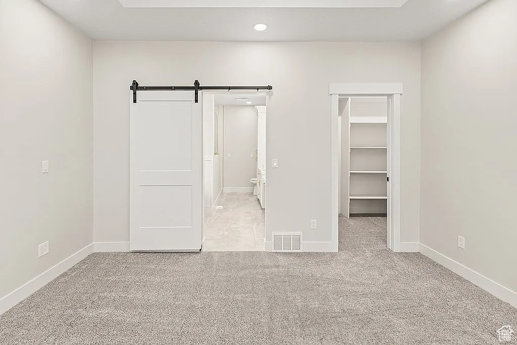 Unfurnished bedroom featuring a barn door, a walk in closet, carpet floors, baseboards, and recessed lighting