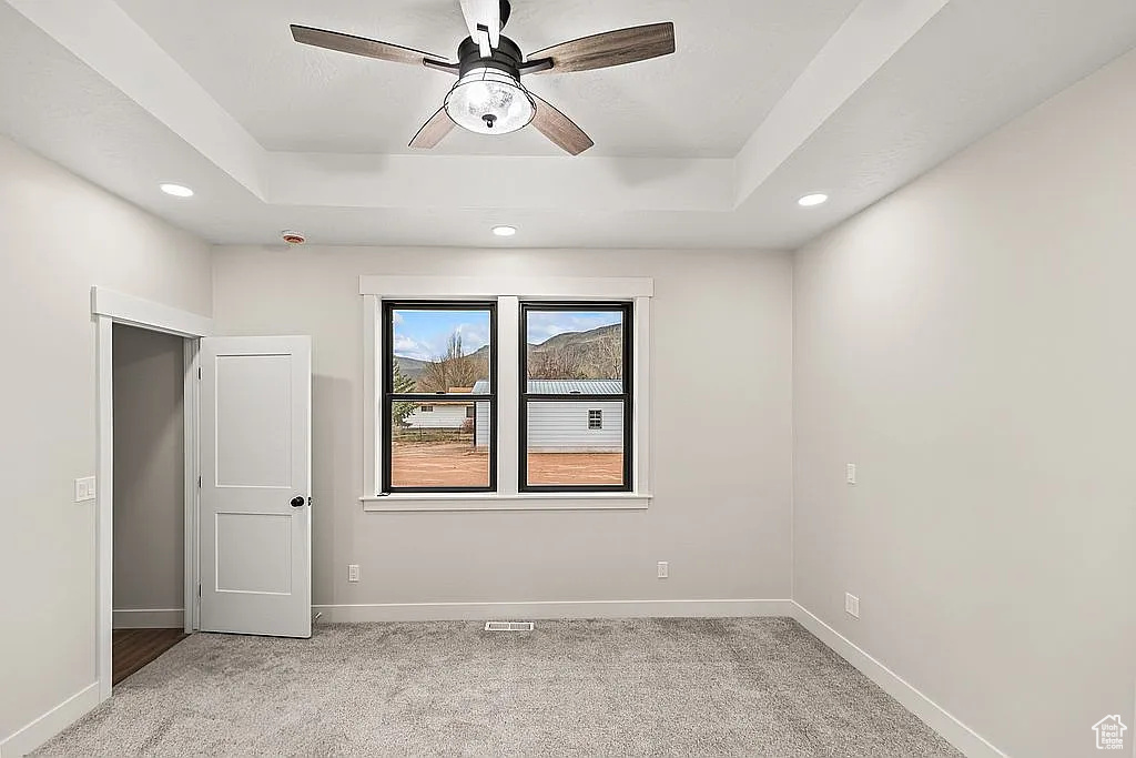 Spare room with a tray ceiling, light carpet, ceiling fan, and recessed lighting