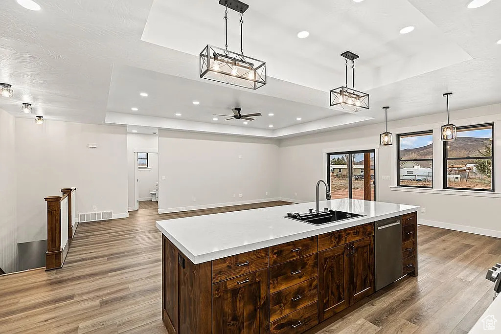 Kitchen with a raised ceiling, a sink, light wood-style flooring, light countertops, and recessed lighting