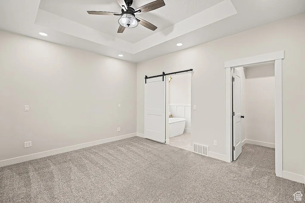 Unfurnished bedroom featuring recessed lighting, a barn door, a spacious closet, carpet floors, and baseboards