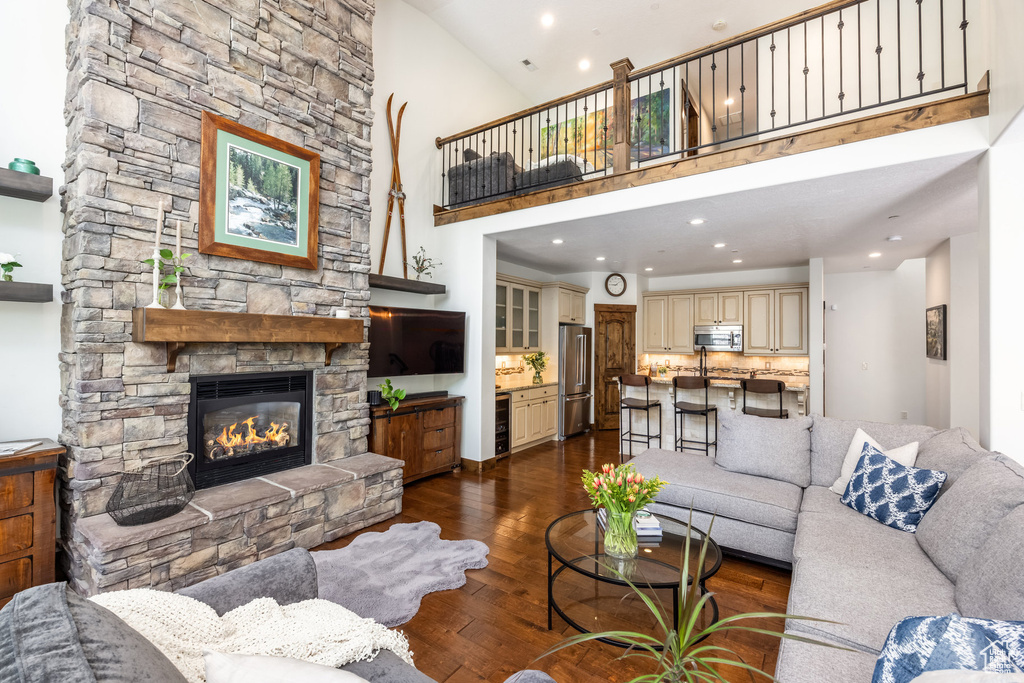 Living room with wine cooler, a fireplace, dark wood-type flooring, a high ceiling, and recessed lighting