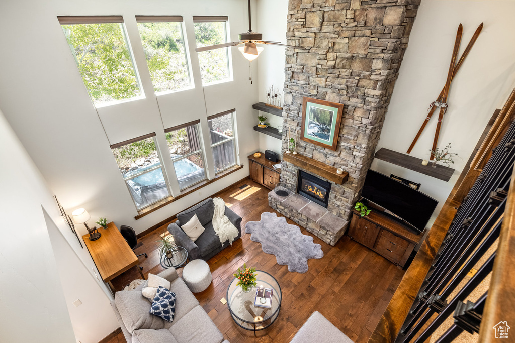 Living room featuring a stone fireplace, hardwood / wood-style floors, a towering ceiling, and ceiling fan