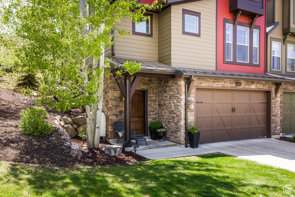 Townhome / multi-family property with a garage, driveway, and stone siding