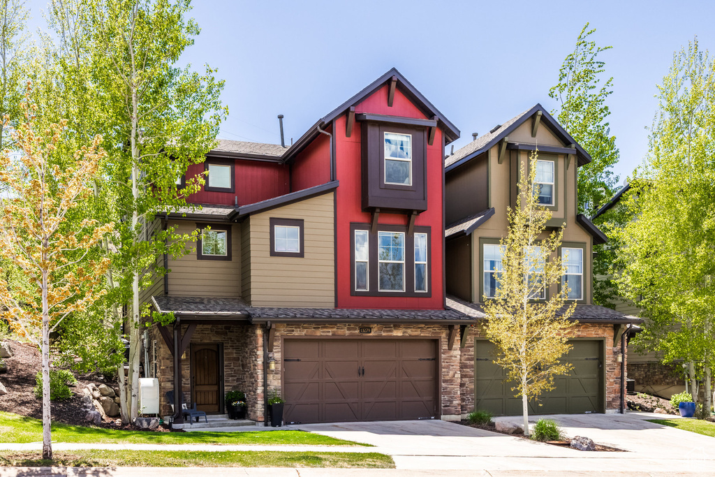 View of front of home featuring an attached garage, concrete driveway, a shingled roof, and stone siding