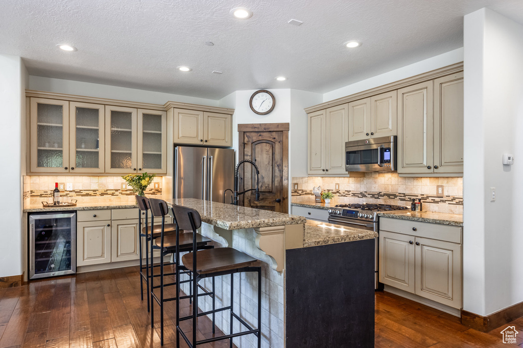 Kitchen with wine cooler, stainless steel appliances, cream cabinetry, dark wood-type flooring, and recessed lighting