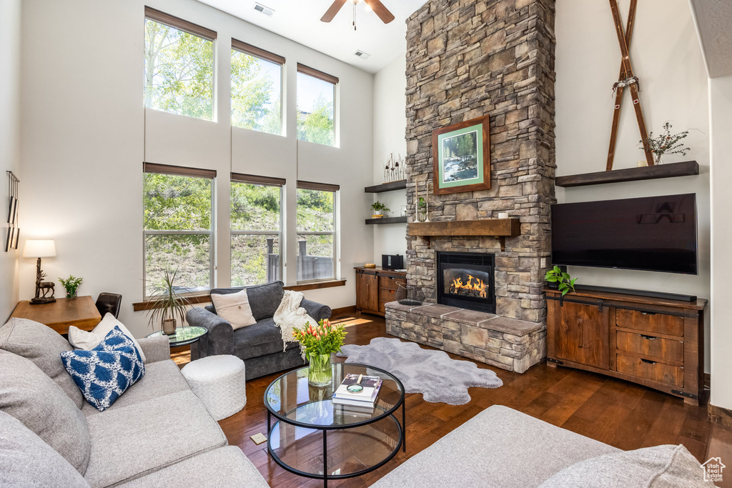 Living area with a ceiling fan, a high ceiling, a stone fireplace, and wood finished floors