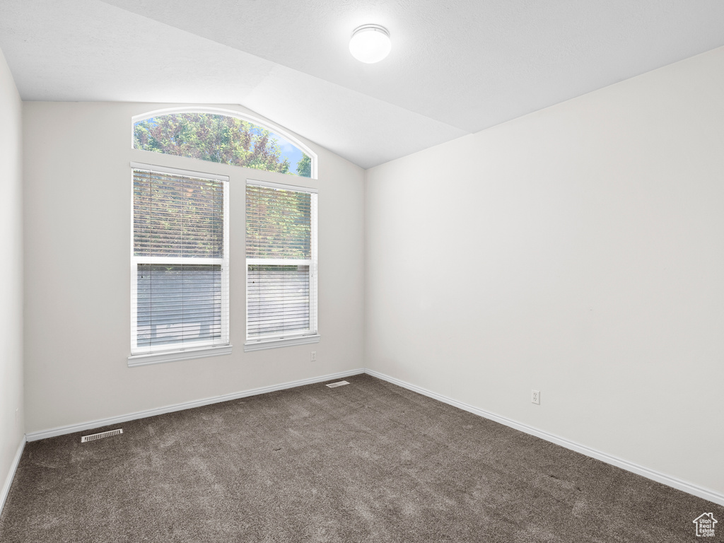 Spare room featuring dark colored carpet, lofted ceiling, and baseboards