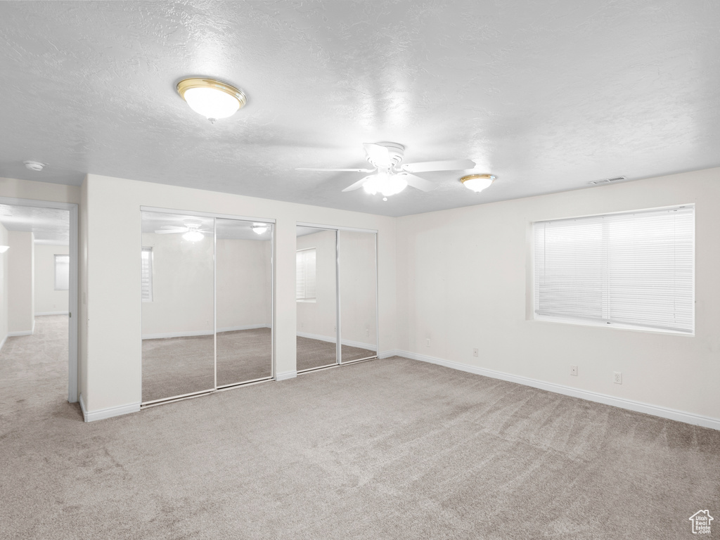Unfurnished bedroom featuring multiple closets, carpet flooring, a textured ceiling, and baseboards