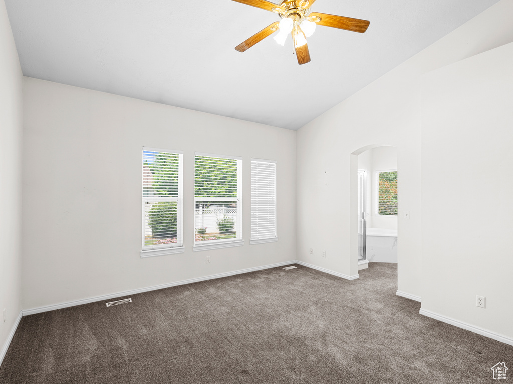 Empty room with arched walkways, carpet floors, ceiling fan, baseboards, and lofted ceiling