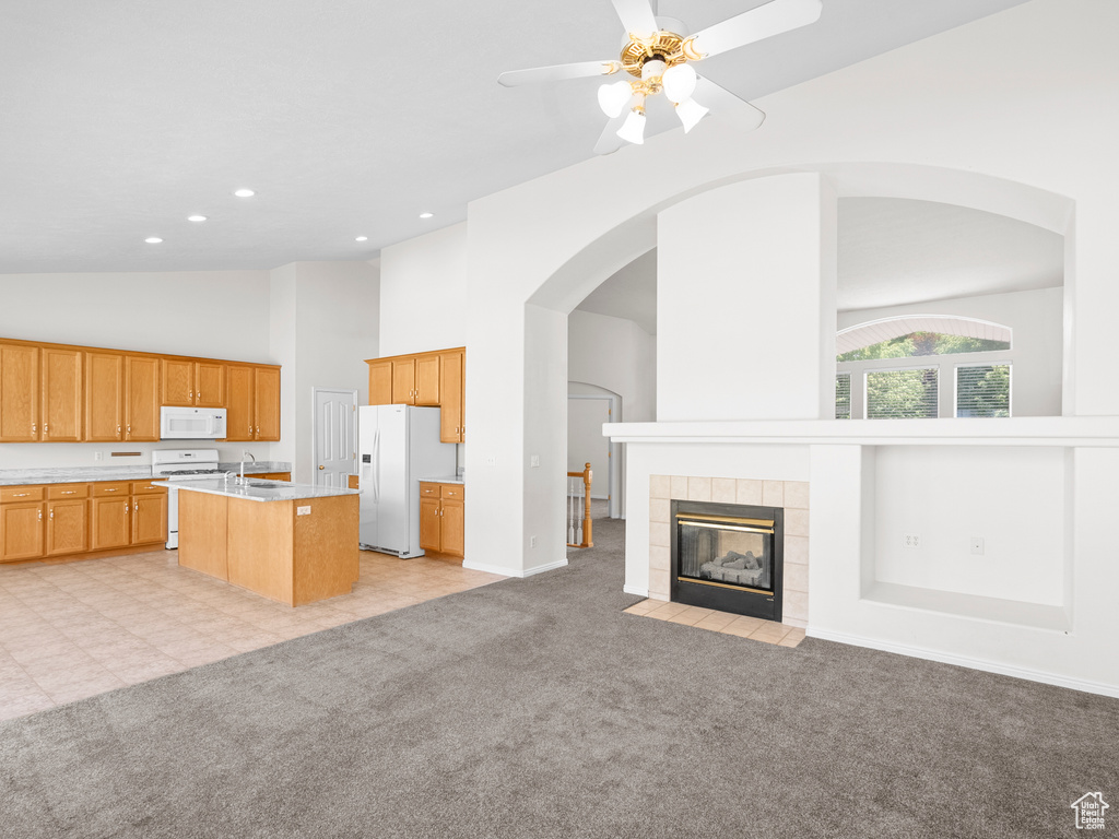 Kitchen with white appliances, open floor plan, high vaulted ceiling, light countertops, and light colored carpet