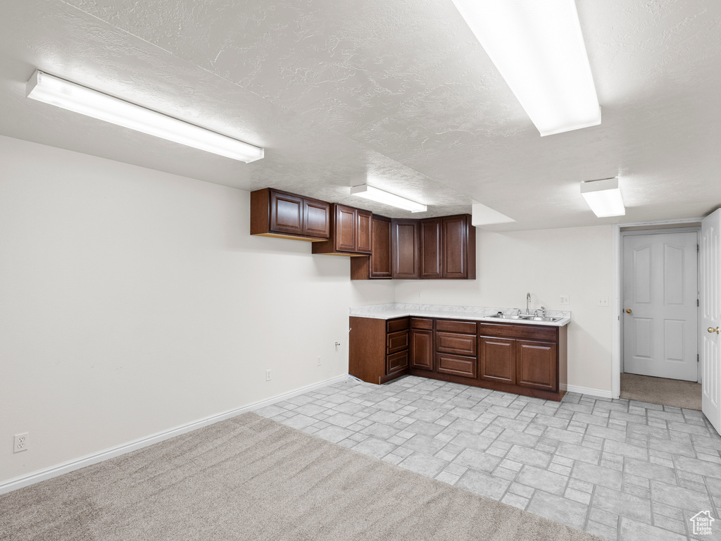 Kitchen with a sink, baseboards, light countertops, dark brown cabinetry, and a textured ceiling