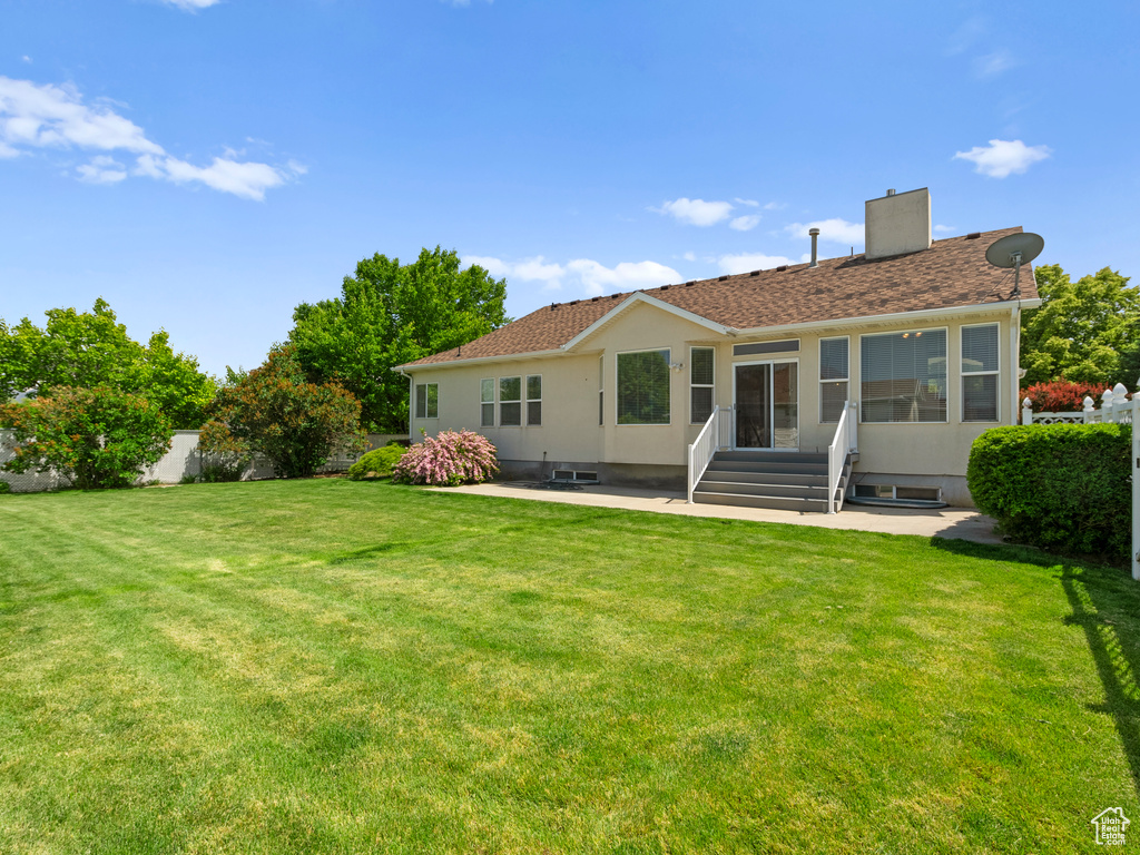 Rear view of property featuring a patio, entry steps, a chimney, a yard, and stucco siding