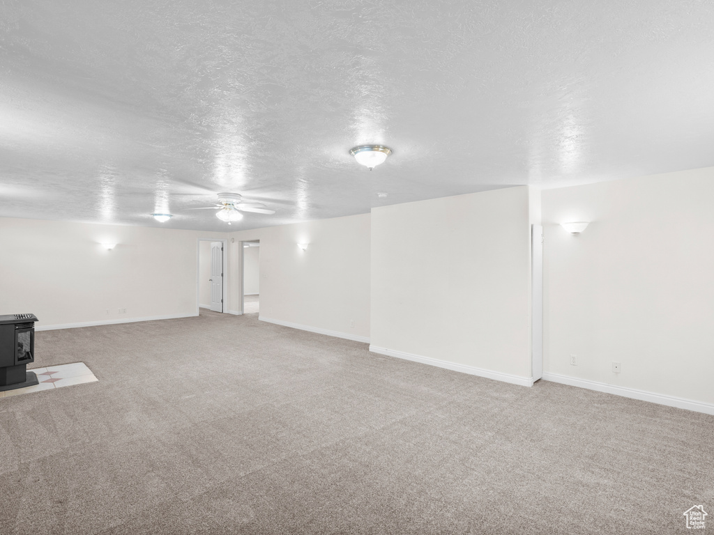 Basement featuring a wood stove, ceiling fan, carpet floors, a textured ceiling, and baseboards
