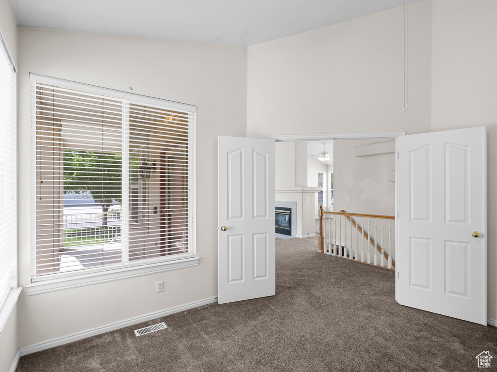 Unfurnished room with carpet floors, high vaulted ceiling, a ceiling fan, a glass covered fireplace, and baseboards