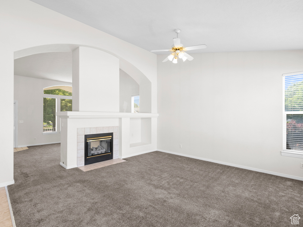 Unfurnished living room featuring healthy amount of natural light, carpet, ceiling fan, and a tile fireplace