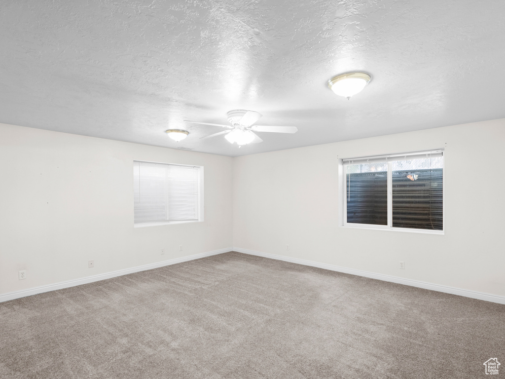 Carpeted empty room featuring a textured ceiling, a ceiling fan, baseboards, and plenty of natural light