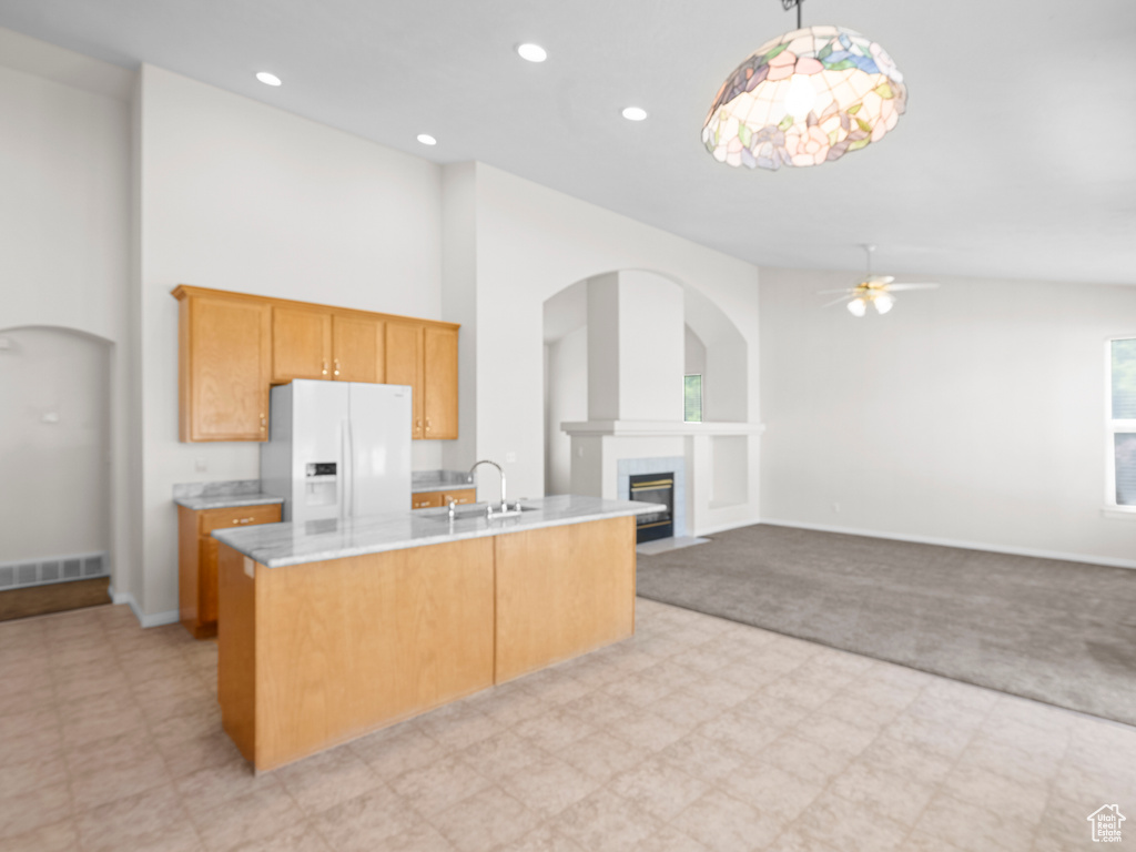Kitchen with white fridge with ice dispenser, ceiling fan, a fireplace with flush hearth, light carpet, and light countertops