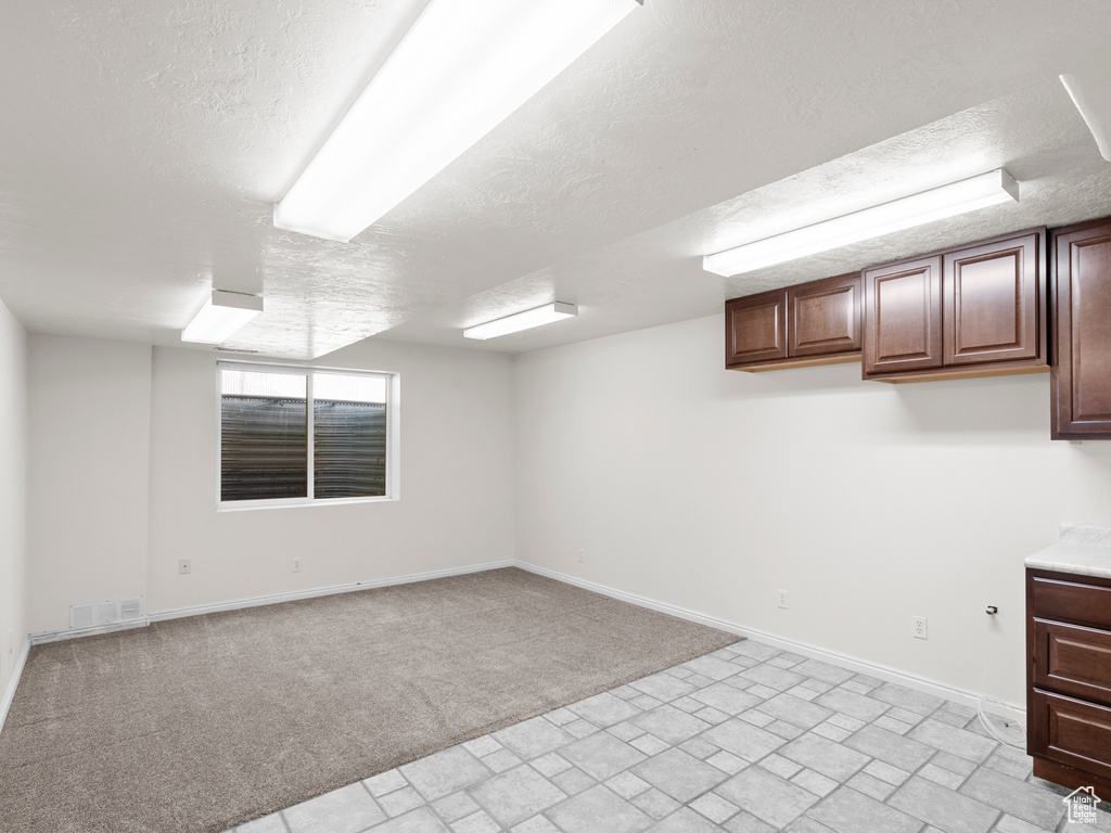 Basement featuring a textured ceiling, baseboards, light carpet, and brick patterned flooring