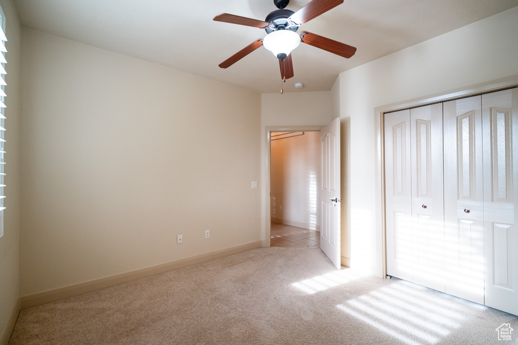 Unfurnished bedroom featuring light colored carpet, a closet, baseboards, and ceiling fan