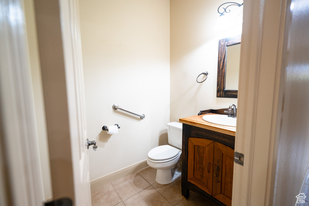 Half bathroom featuring toilet, vanity, tile patterned floors, and baseboards