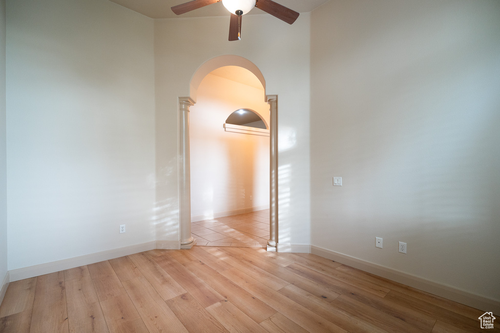 Empty room with arched walkways, ceiling fan, light wood finished floors, and baseboards