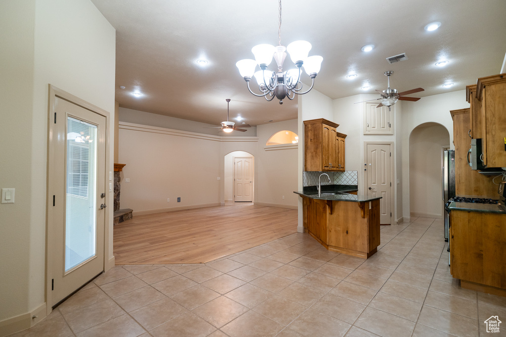 Kitchen featuring arched walkways, a ceiling fan, brown cabinetry, light tile patterned floors, and recessed lighting