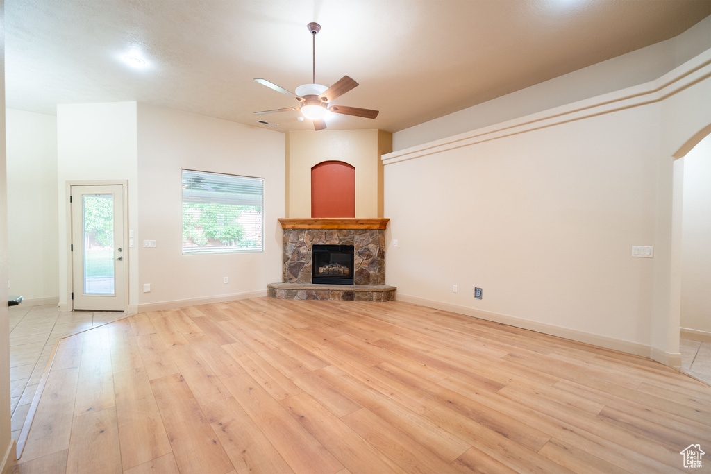 Unfurnished living room featuring ceiling fan, light wood finished floors, a fireplace, arched walkways, and baseboards
