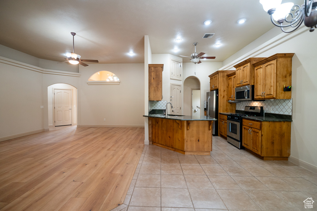 Kitchen with stainless steel appliances, ceiling fan, arched walkways, brown cabinets, and recessed lighting