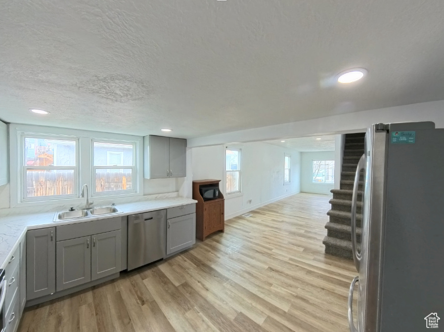Kitchen with stainless steel appliances, a sink, gray cabinets, light wood finished floors, and a textured ceiling
