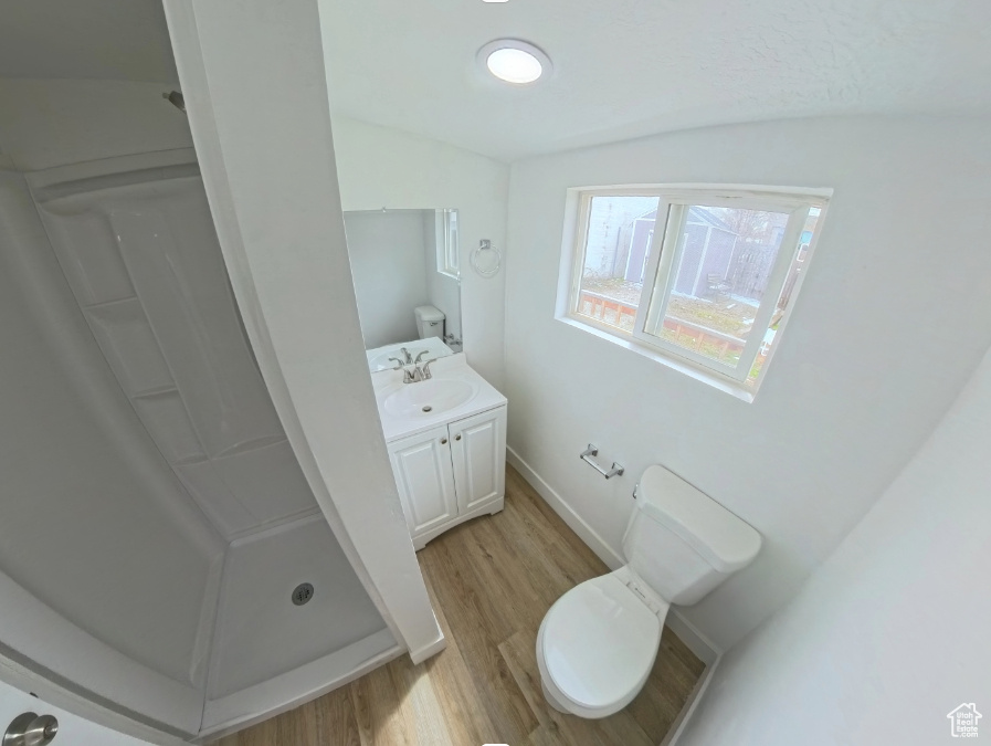 Bathroom featuring a stall shower, wood finished floors, vanity, toilet, and vaulted ceiling
