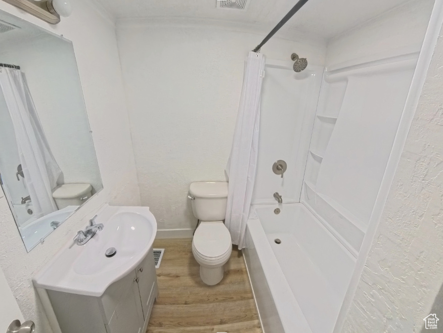 Bathroom with wood finished floors, vanity, toilet, shower / bath combo, and a textured wall