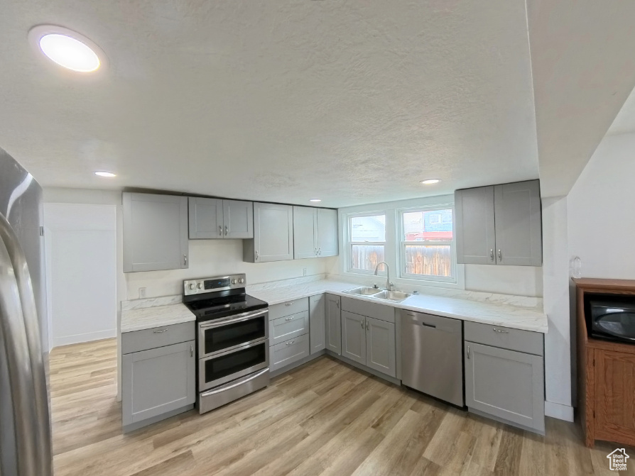 Kitchen with gray cabinetry, appliances with stainless steel finishes, a sink, light wood-style floors, and recessed lighting