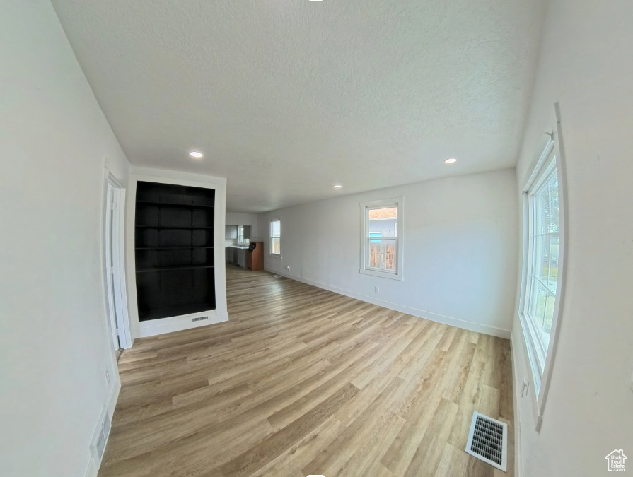 Unfurnished living room with light wood finished floors, a textured ceiling, recessed lighting, and baseboards