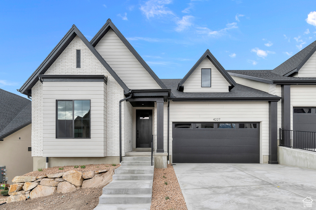 View of front of house featuring a garage, concrete driveway, and roof with shingles