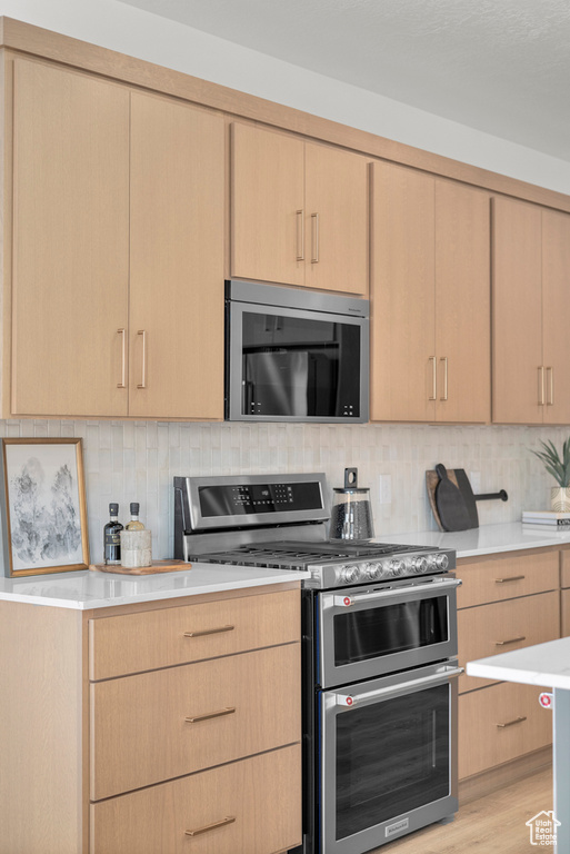 Kitchen with appliances with stainless steel finishes, light brown cabinetry, light countertops, and backsplash