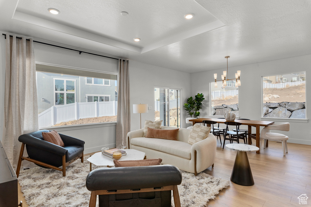Living area with a chandelier, light wood-type flooring, a raised ceiling, healthy amount of natural light, and recessed lighting