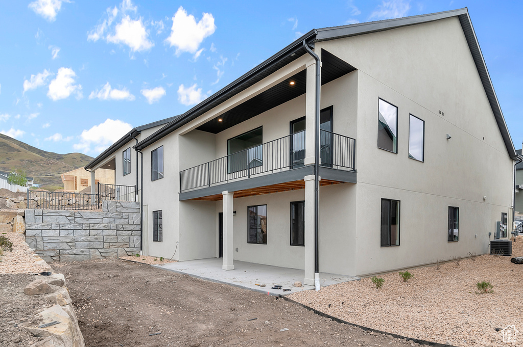 Back of house featuring stucco siding, a balcony, a patio area, central AC unit, and a mountain view
