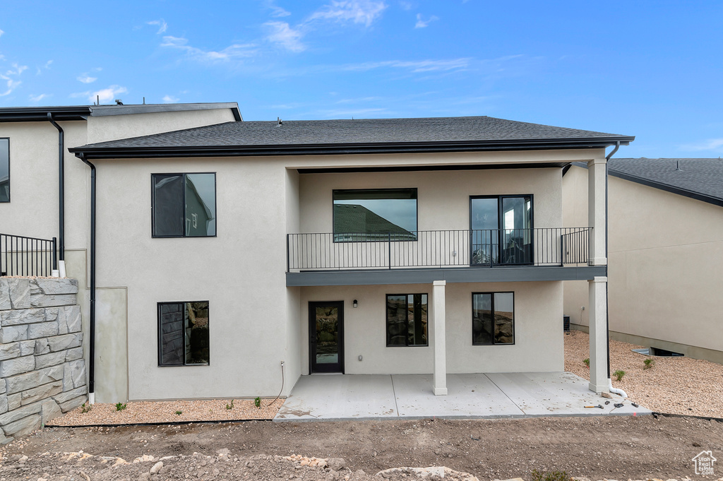 Back of house featuring a balcony, a patio, stucco siding, and a shingled roof