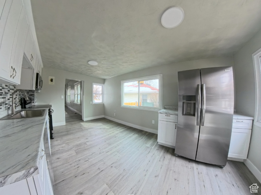 Kitchen featuring stainless steel appliances, a sink, light wood-style flooring, backsplash, and white cabinets
