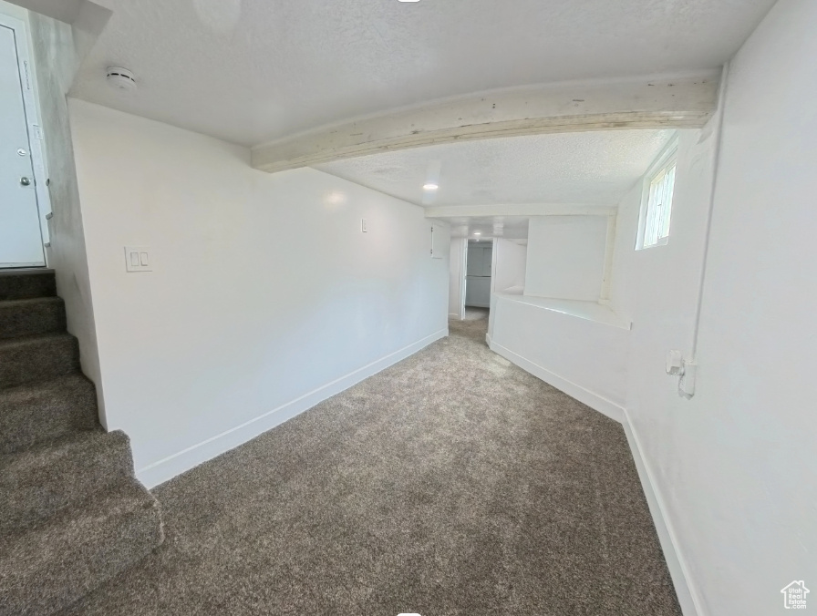 Below grade area featuring carpet floors, baseboards, stairway, and a textured ceiling