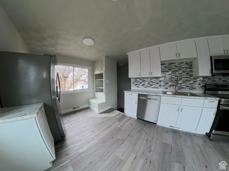 Kitchen with stainless steel appliances, white cabinetry, baseboards, and backsplash