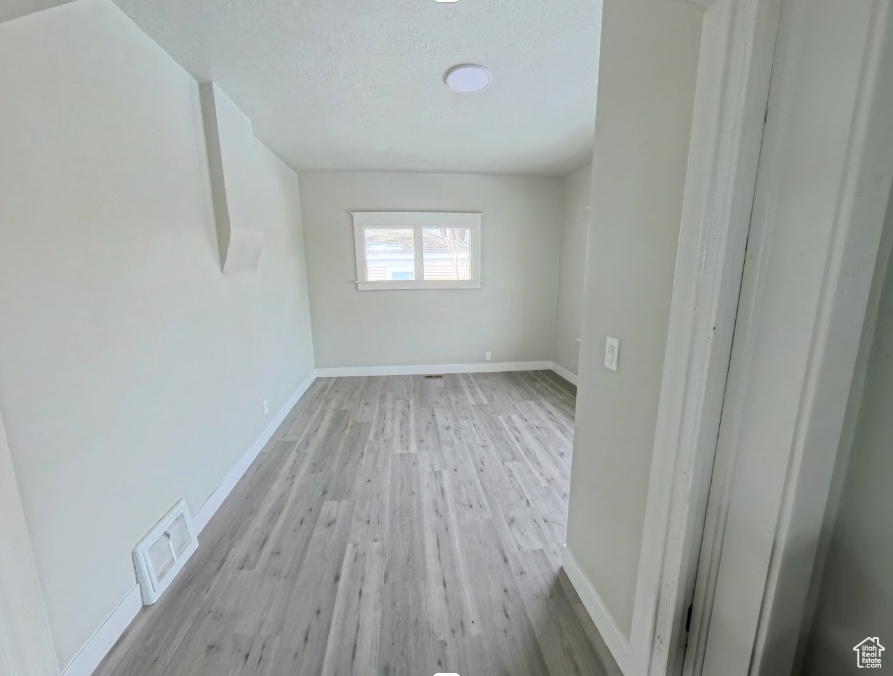 Unfurnished room with light wood finished floors, baseboards, and a textured ceiling