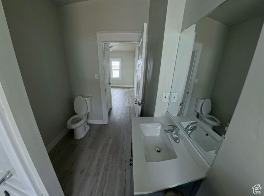 Half bath featuring toilet, wood finished floors, vanity, and baseboards