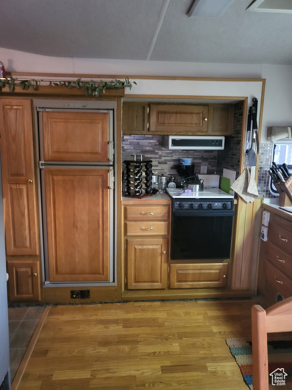 Kitchen with stove, range hood, tasteful backsplash, and light wood-type flooring