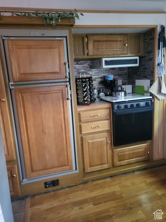 Kitchen with electric stove, tasteful backsplash, ventilation hood, light countertops, and brown cabinets