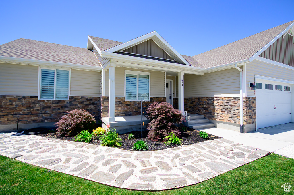 Craftsman-style house with stone siding, a porch, board and batten siding, an attached garage, and a shingled roof
