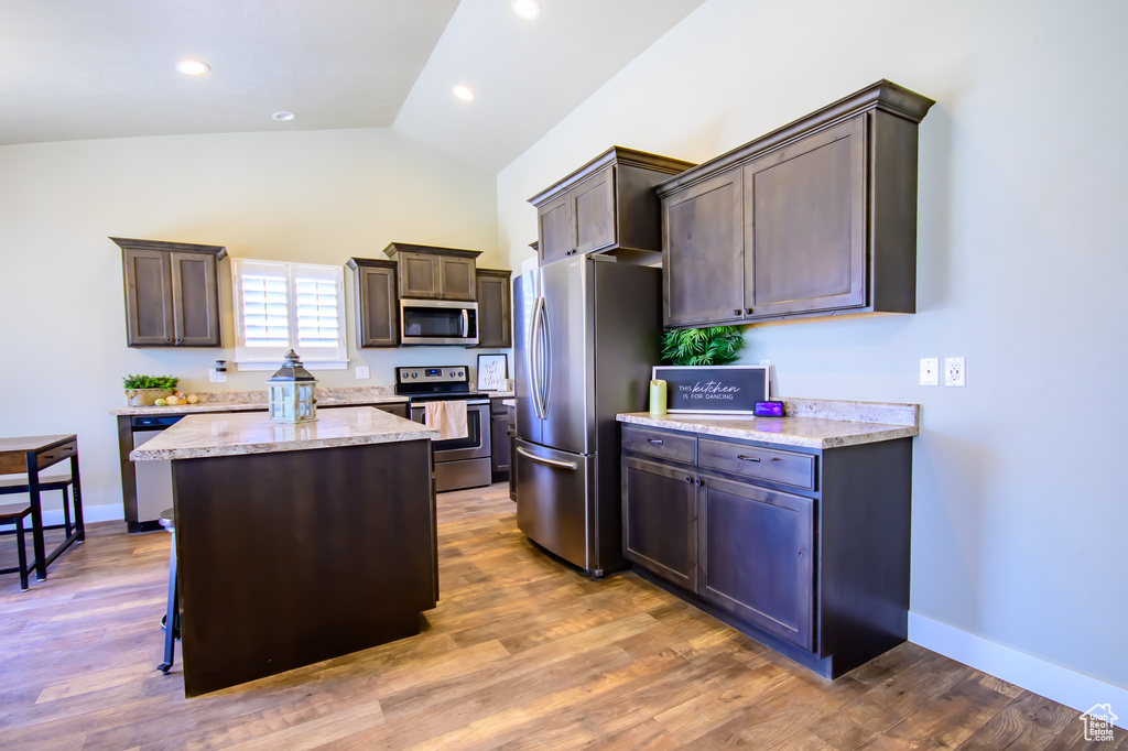 Kitchen featuring appliances with stainless steel finishes, lofted ceiling, a kitchen island, dark brown cabinetry, and baseboards