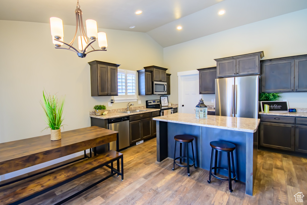 Kitchen featuring stainless steel appliances, a center island, a sink, light stone countertops, and lofted ceiling