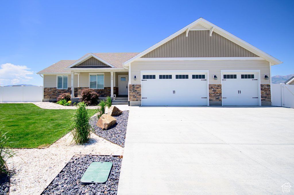 Craftsman house featuring an attached garage, stone siding, driveway, board and batten siding, and roof with shingles